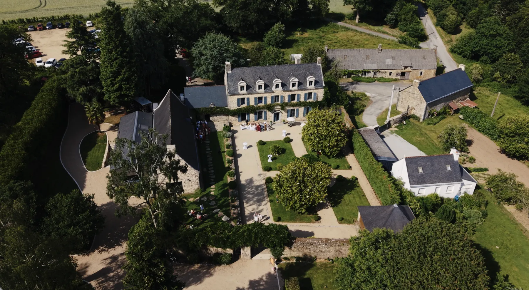 Vue aérienne du Manoir de Gouézac à Grand-Champ dans le Morbihan, le jour du mariage de Chloé et Sylvain : le manoir en pierre claire, ses dépendances et le jardin à la française.