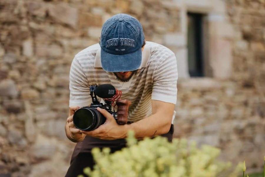 Simon Blanchet, vidéaste de mariage, caméra et micro en main devant un mur de pierre.